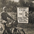 A passing despatch rider reads a beachhead sign warning against butterfly bombs, Normandy, 1944