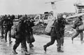 Argentine prisoners of war pass a wrecked Pucara ground attack aircraft, Goose Green, Falklands, 1982