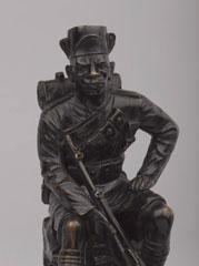 Statuette of an askari of the King's African Rifles in marching order, seated on a rock, 1922