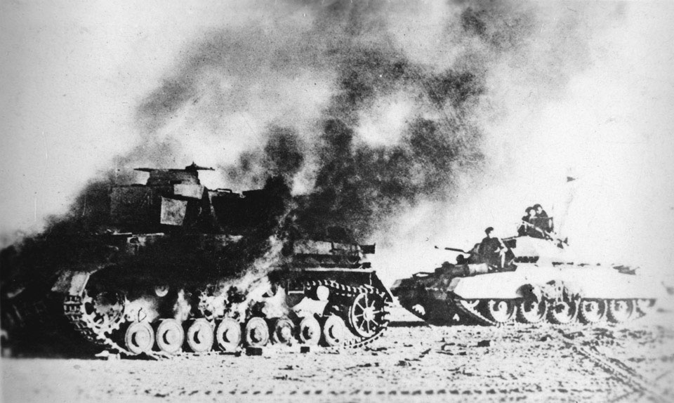 A British Crusader tank passes a burning German Pzkw Mk IV during Operation Crusader, November 1941