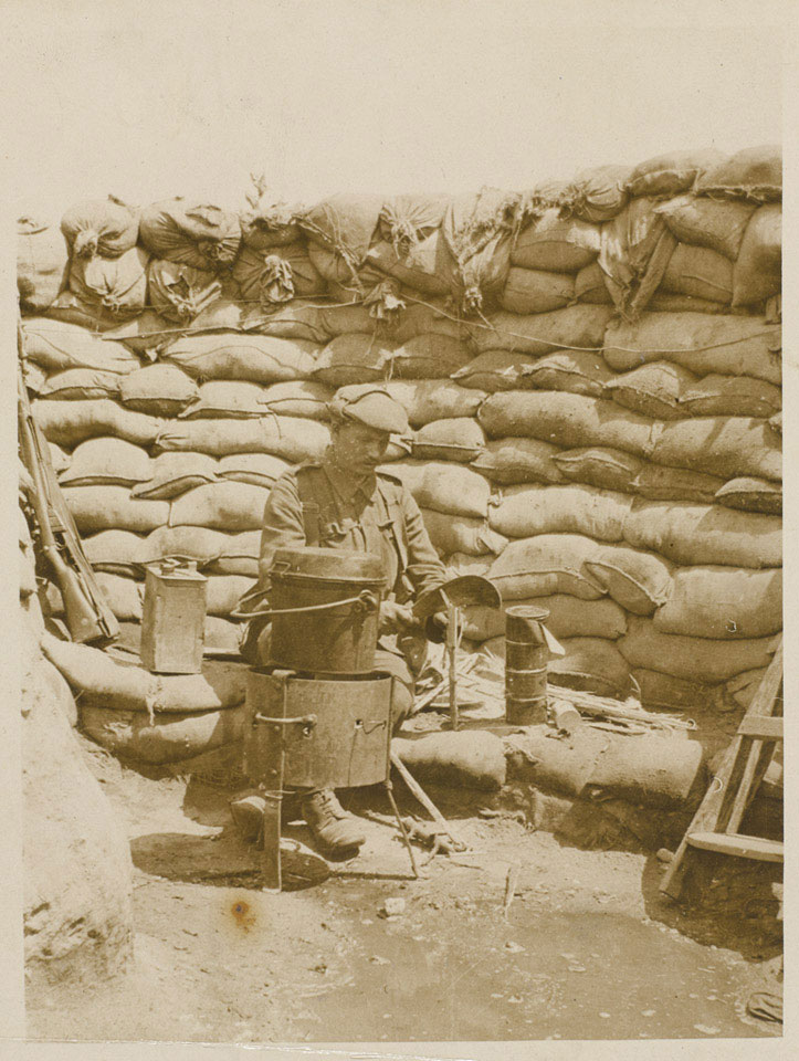 A cook preparing food in a dixie on a charcoal fire at the front, 1915