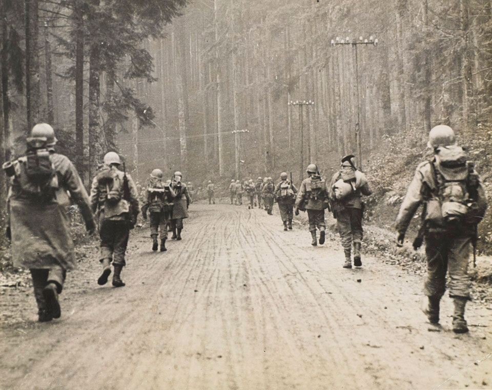 US 7th Army infantryman march through a forest, 1945